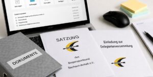 Auf einem Tisch liegen vor einem Laptop eine Satzung, ein Ordner und eine Einladung zur Delegiertenversammlung