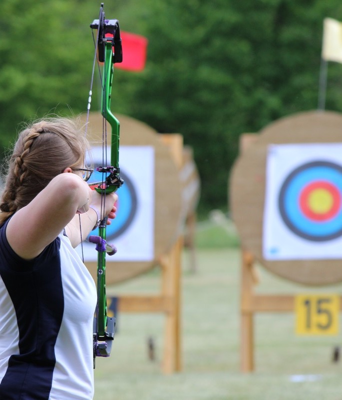 Eine Frau schießt auf einem Sportplatz auf eine Scheibe mit mehrfarbigen Auflagen