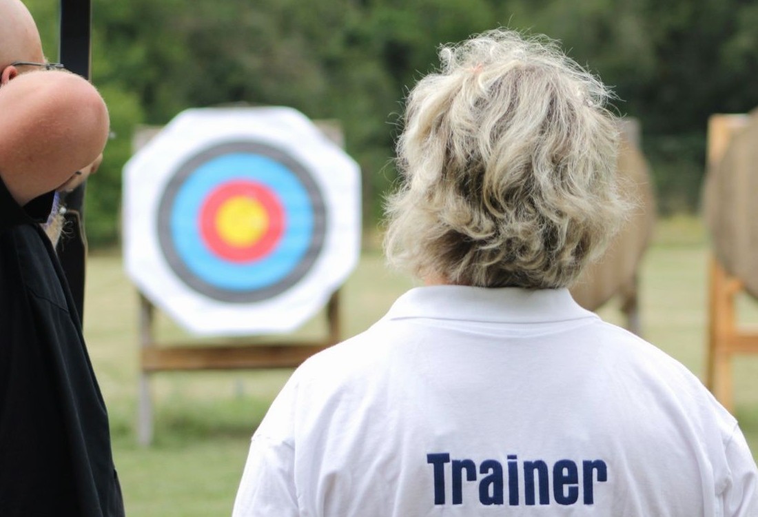 Trainer steht neben einem Bogenschützen