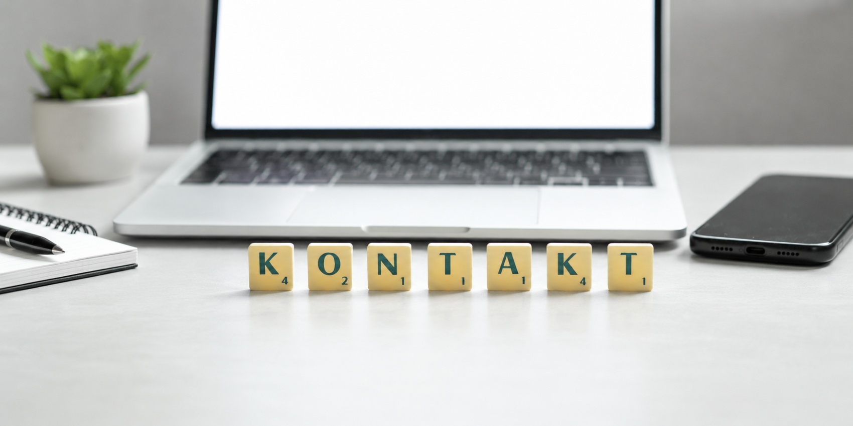 Buchstaben aus dem Spiel Scrabble bilden das Wort Kontakt und stehen vor einem Laptop und einem Smartphone