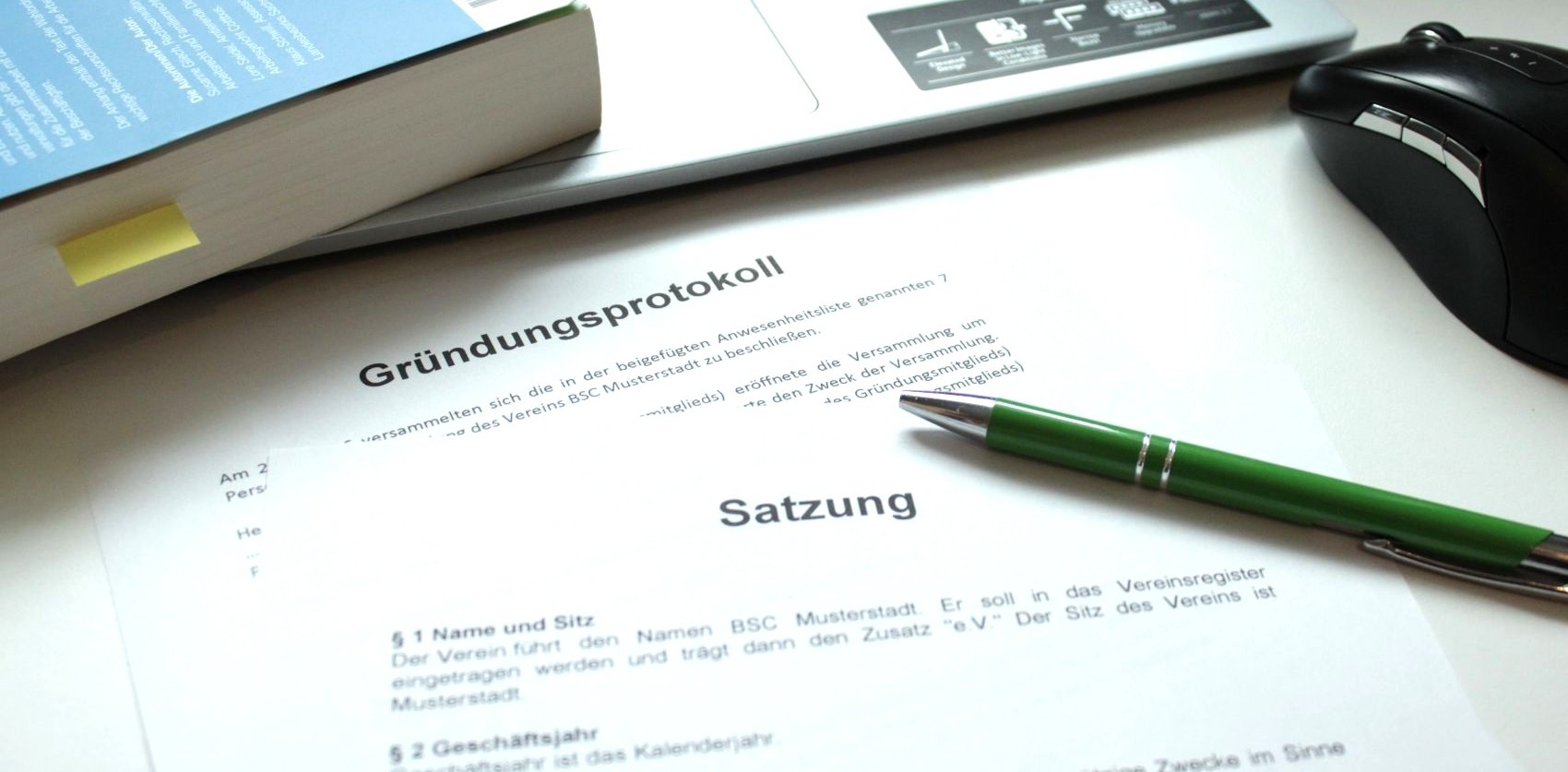 Ein Gründungsprotokoll und eine Satzung liegen von einem Laptop