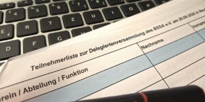 Eine Teilnehmerliste einer Versammlung liegt auf der Tastatur eines Laptops